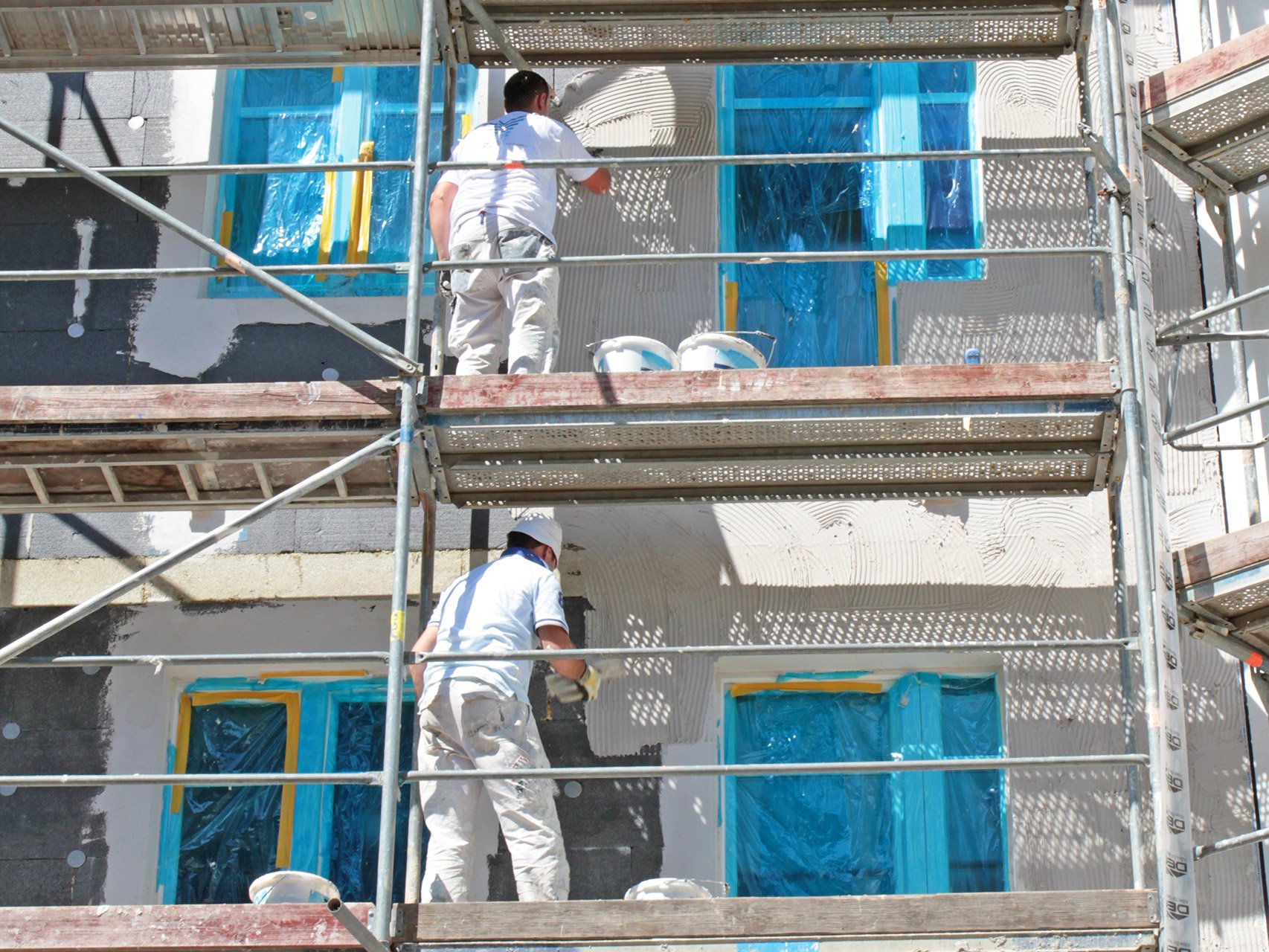 Zwei Männer auf einem Gerüst. Sie verputzen die Wand.